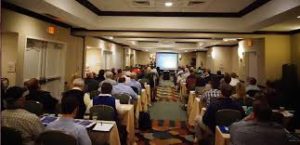 Conference attendees seated facing a presentation screen.